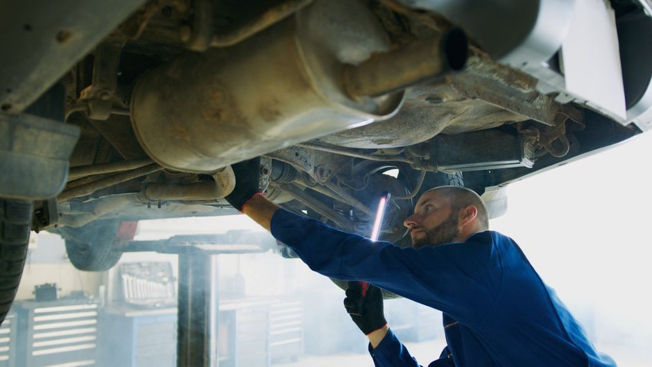 Technician discussing repair work with a customer beside a car on a ramp in a clean workshop